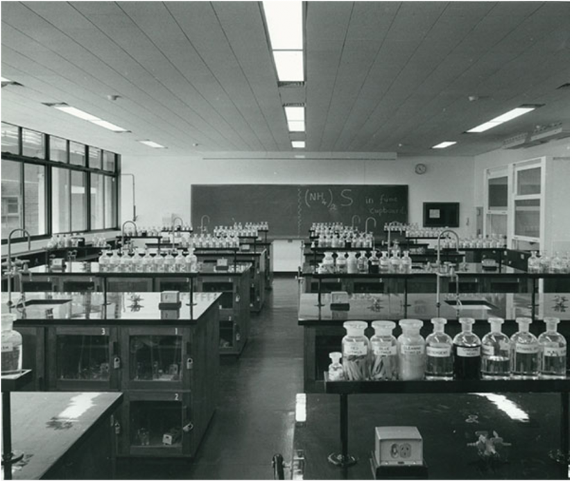 Lines of desks with jars on top looking towards a blackboard