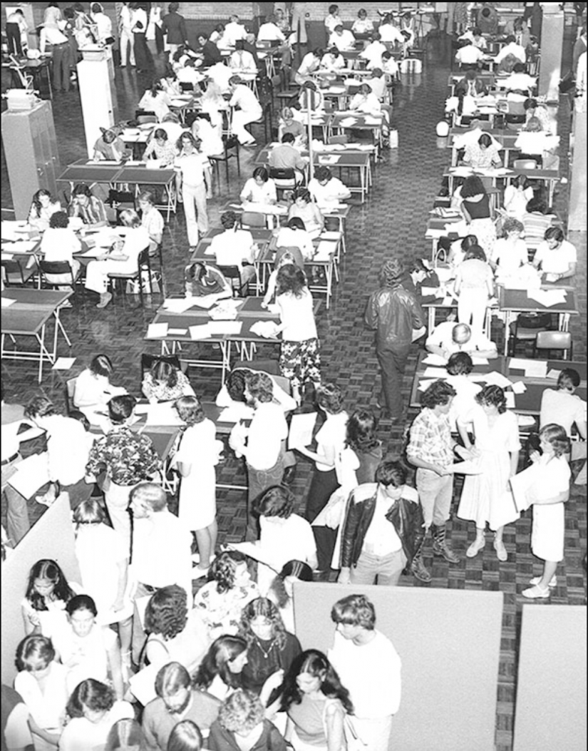 Black and white image of rows of desks and people lining up to enrol