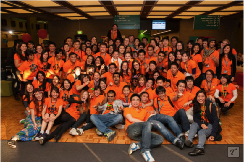 Group of 50 or more people smiling at the camera, wearing orange shirts