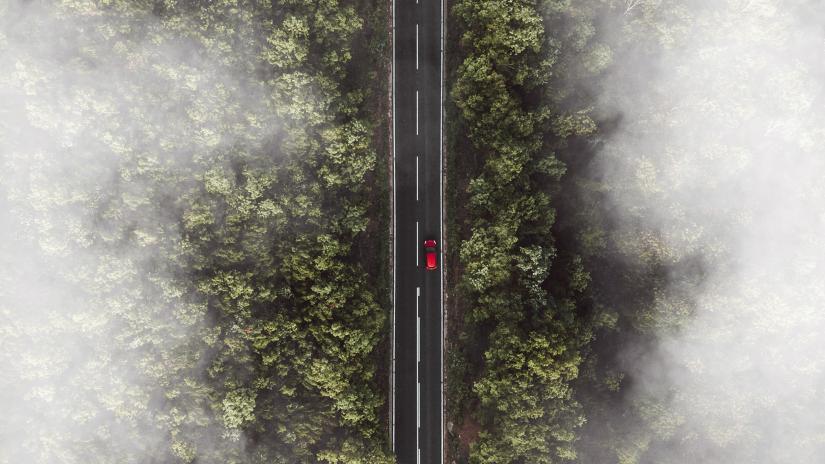 Aerial photo of a forest. A road runs through the centre, with a red car driving along it.