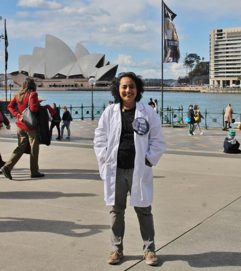 Woman in lab coat in front of Sydney Opera House