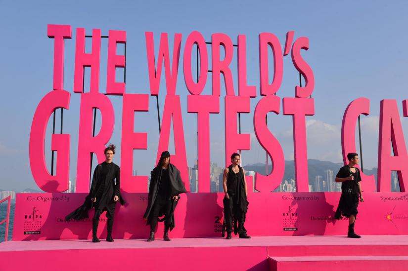 Four models wearing black stand on a bright pink stage