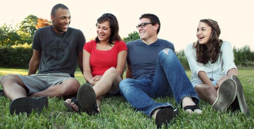 Four people sitting on grass, smiling at each other