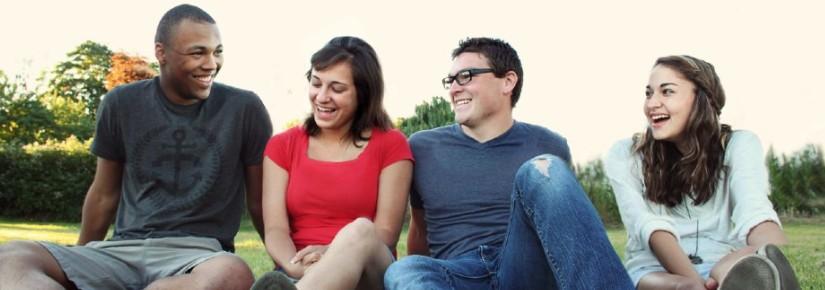 Four people sitting on grass, smiling at each other