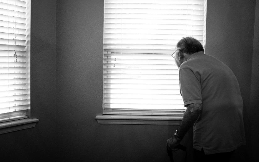 An elderly man in a white room near two windows.