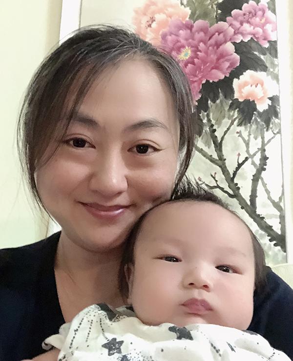 Min faces the camera, smiling and holding her baby in the foreground