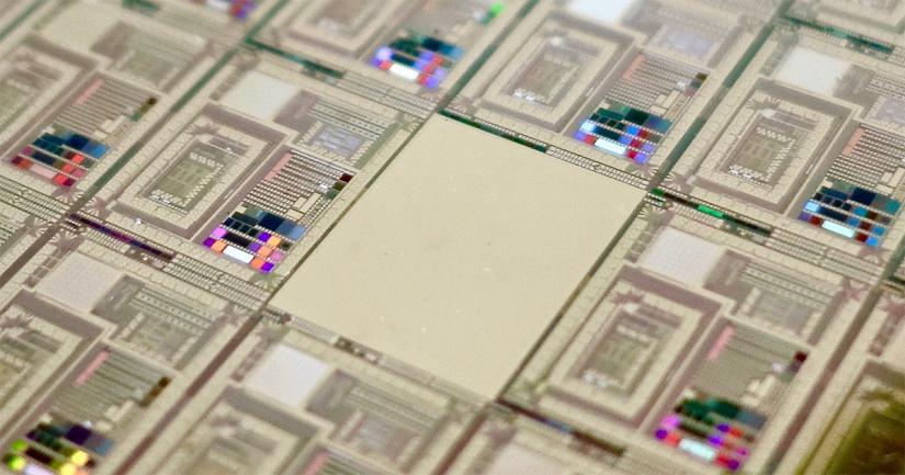 A close-up of the D-Wave Vesuvius chip. Image shows many rectangular gold metallic sections joined together with colourful sections in the lower left corner of each rectangle. The centre rectangle does not contain anything, only the gold metallic colour