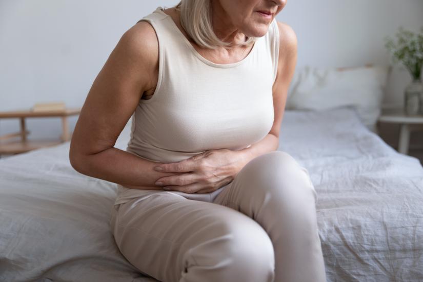 Older lady sitting on bed with hands over abdomen