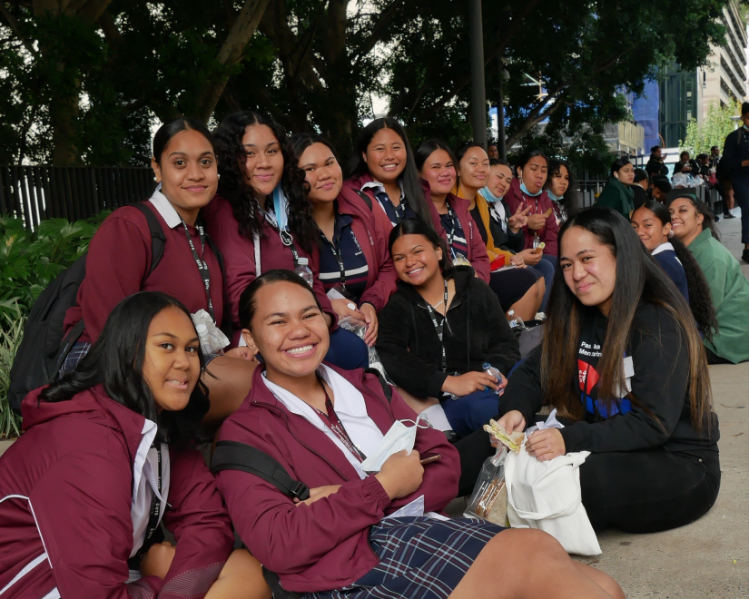 group photo of high school girls sitting together outside, smiling at the camera