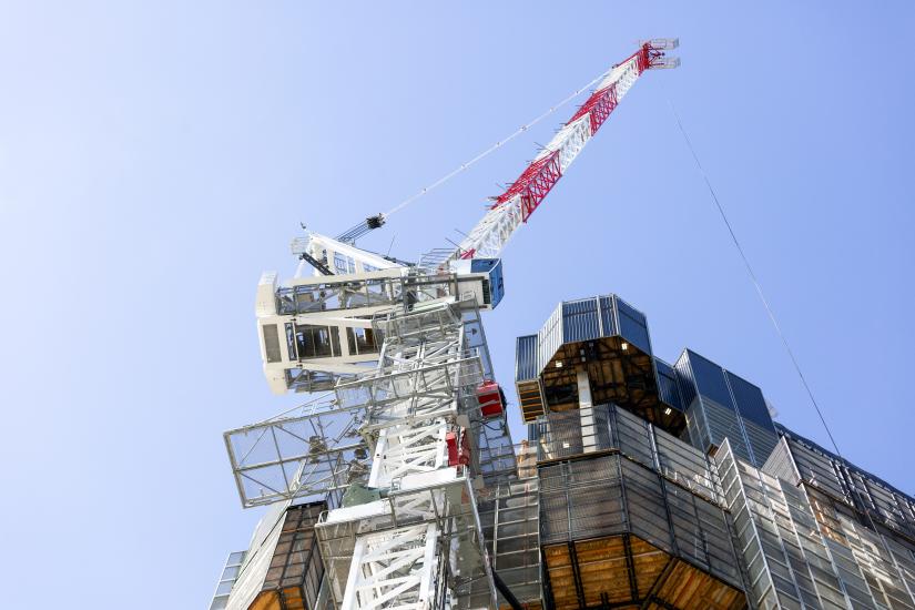 A red and white crane is seen from below with some construction in the foreground