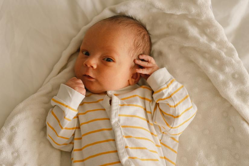 Baby in yellow and white striped jumpsuit lies on a white textured blanket