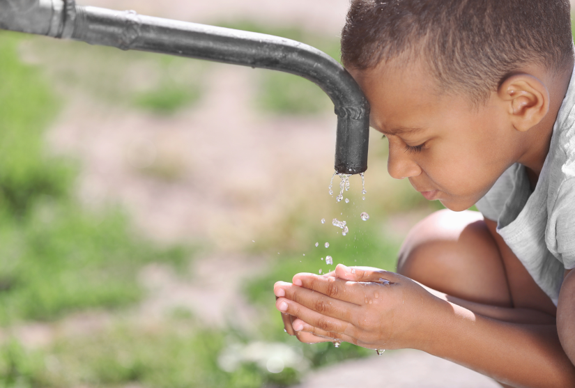 Young boy cupping his hands below a tap dripping water and his face is pressed against the tap