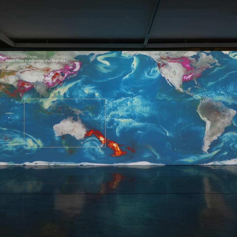 A large projected image of a world map. The east coast of Australia is on fire