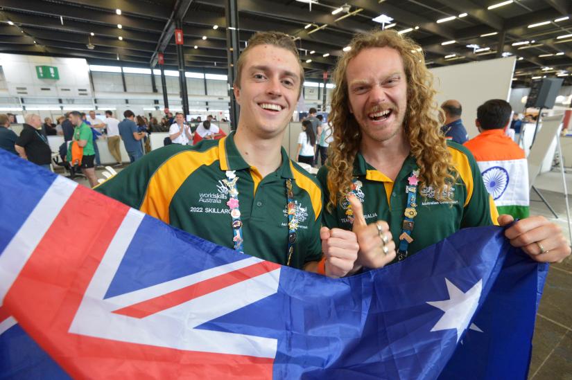 Daniel Gardner and Christopher Brown hold an Australian flag and give thumbs up at WorldSkills competition