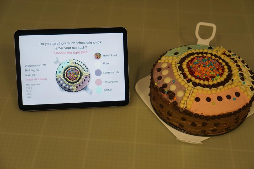 Cake decorated in segments with coloured icing and chocolate pieces next to iPad explaining the idea:"Do you care how many chocolate chips enter your stomach?"