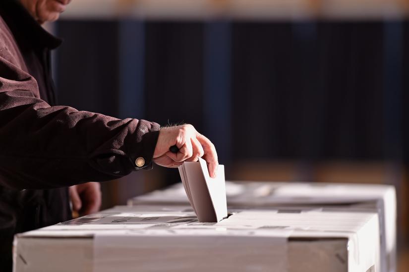 an older person places a voting paper in a polling box