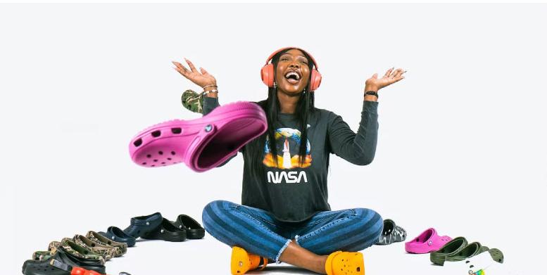 A woman sits smiling, surrounded by crocs
