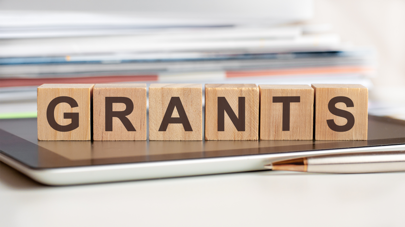 'GRANTS' spelled out on wooden blocks in capital letters. The blocks are sitting on a closed laptop computer.