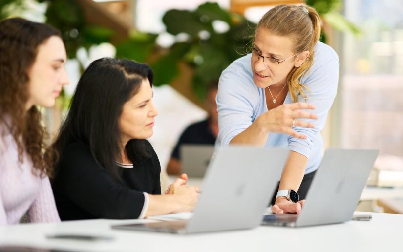 Two students looking at Apple laptops while a course instructor points to the screen.