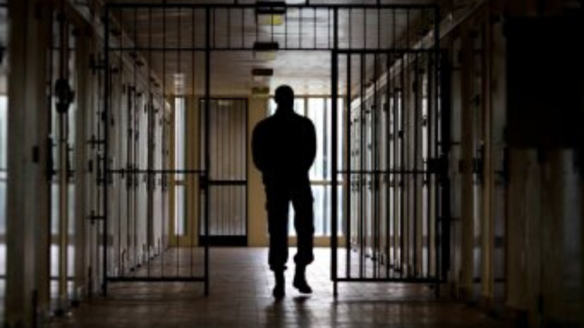 Silhouette of man walking through prison corridor. There are gates with bars. 