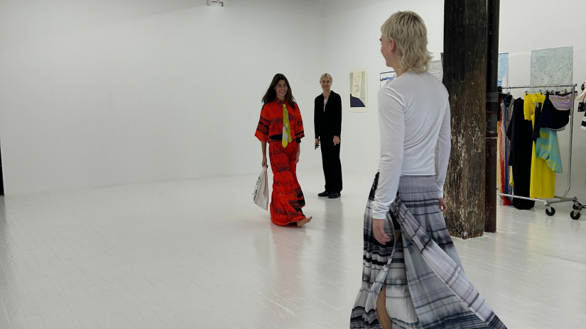 Three fashion models practice walking the runway in Alix Higgins' creations at a fitting in a white room