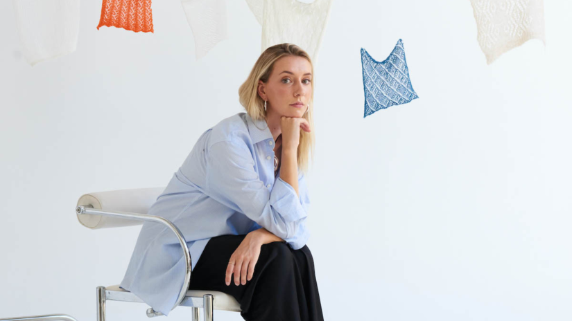 Cameron Hill sitting on a chair in front of hanging pieces of fabric