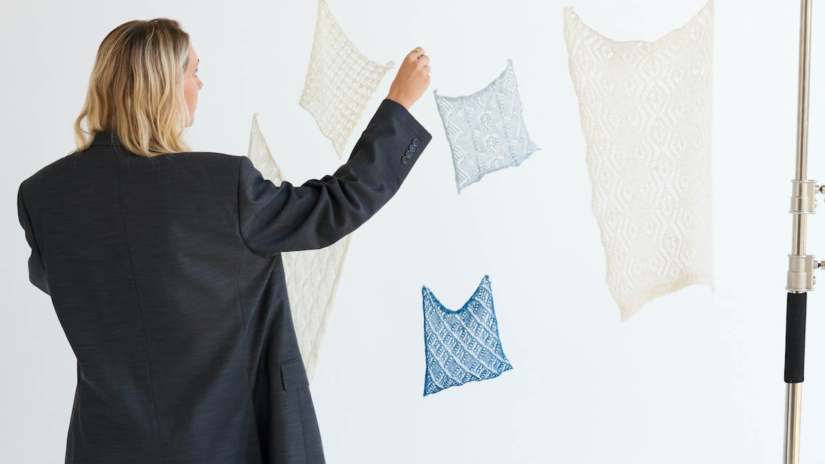 Cameron Hill stands with back to camera adjusting hanging pieces of fabric in a white studio
