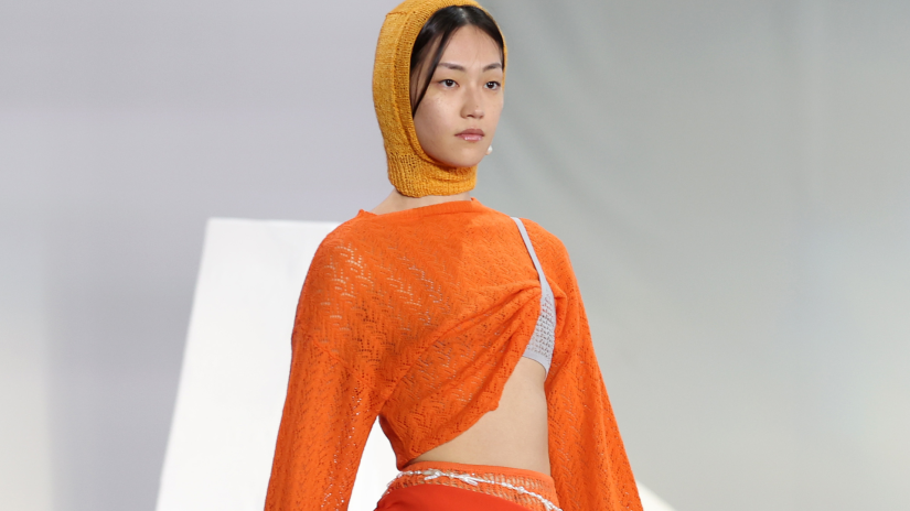 Fashion model on the runway wearing an orange top, skirt and head scarf designed by Cameron Hill