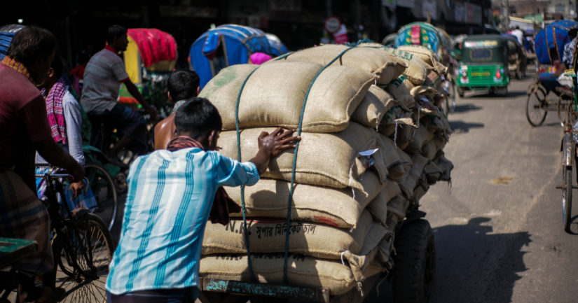 A labor pushing a two wheeler cart full of rice sacks in street of Dhaka Bangladesh