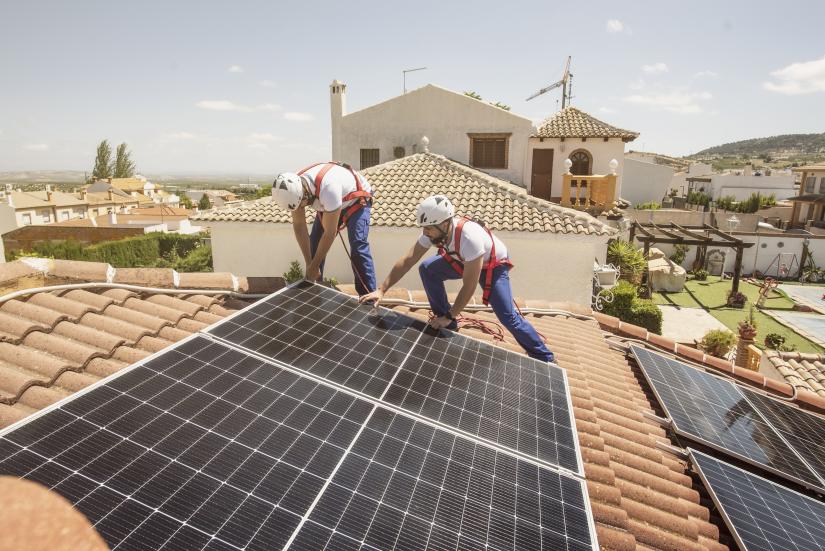 Two workmen install solar panels on a suburban rooftop