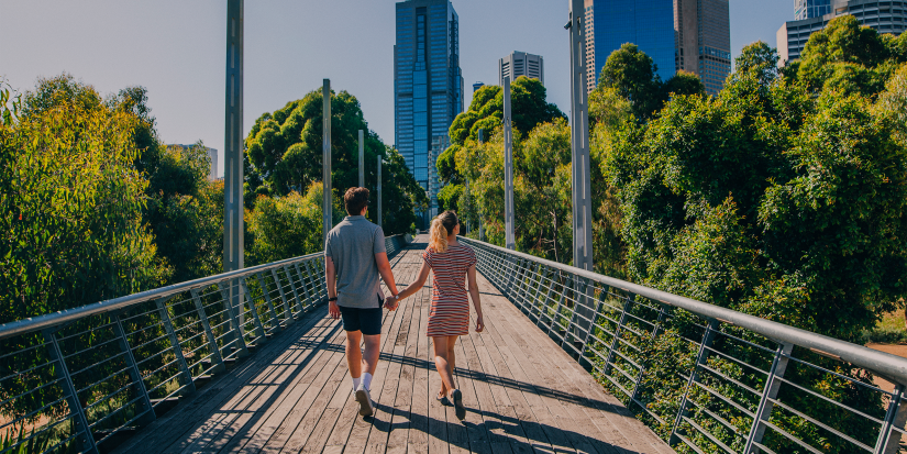 A young couple holding hands, walking down a bridge