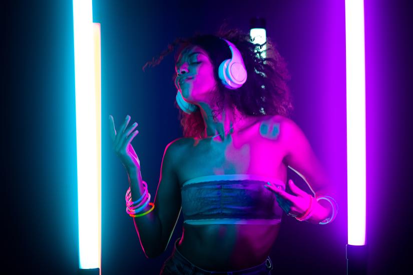 A woman with white headphones over her head dancing in neon lights