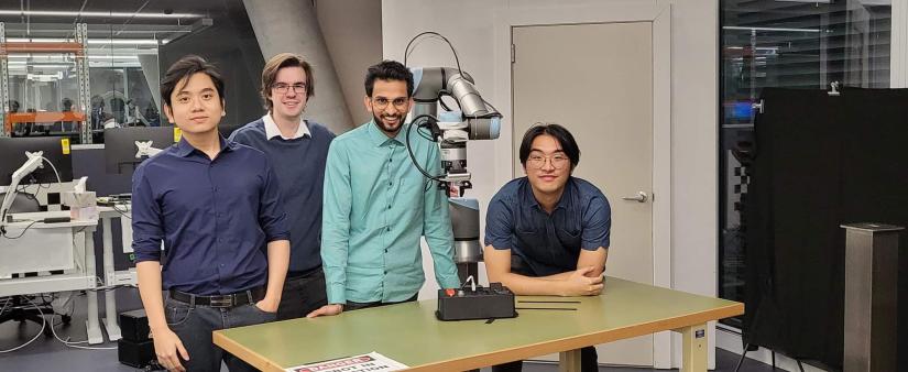 Four male students standing at a desk behind a robotic arm.