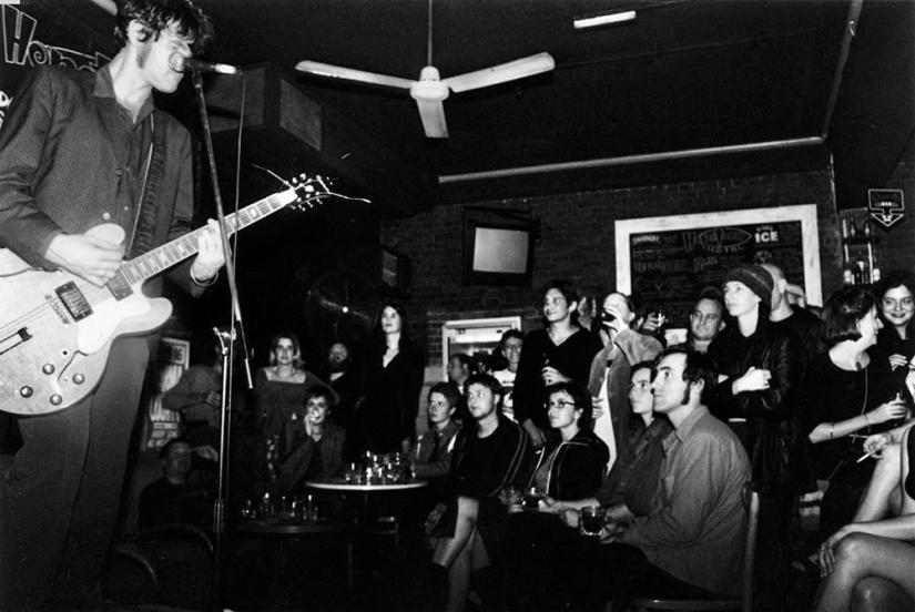 A man sings and plays guitar while a crowd watches on intently