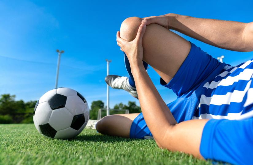 Footballer lying on the ground holding his knee.