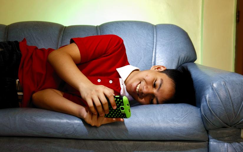Stock picture of a smiling teen looking at a smartphone lying on a couch.