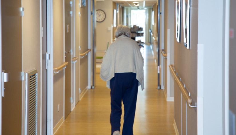 Elderly woman walking down hallway in retirement home.