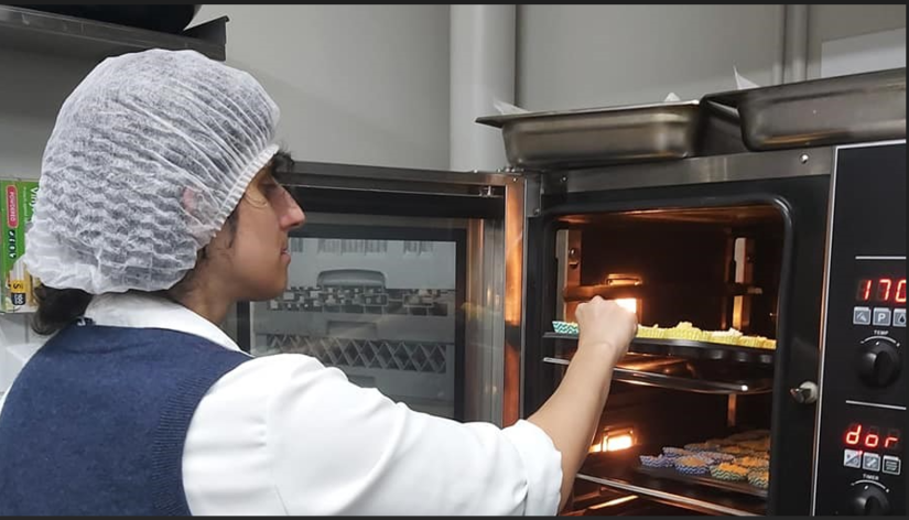 Catarina with wig on, putting food in a commercial oven
