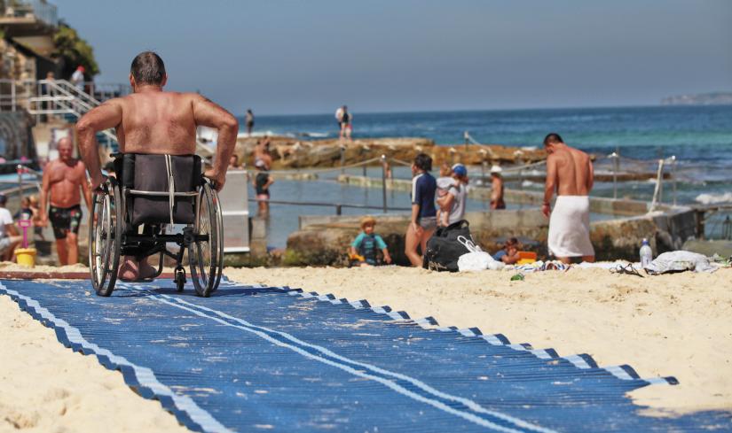 Photo of person in wheelchair going across a mat on the beach