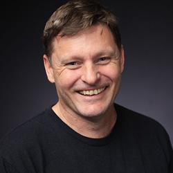 Man with short brown hair smiling and look at the camera in a black tshirt