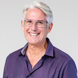 Man with short grey hair and glasses smiling and looking at the camera in a purple button up shirt