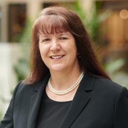 Woman with long hair and a fringe wearing a black suite jacket and black shirt smiling and looking at the camera