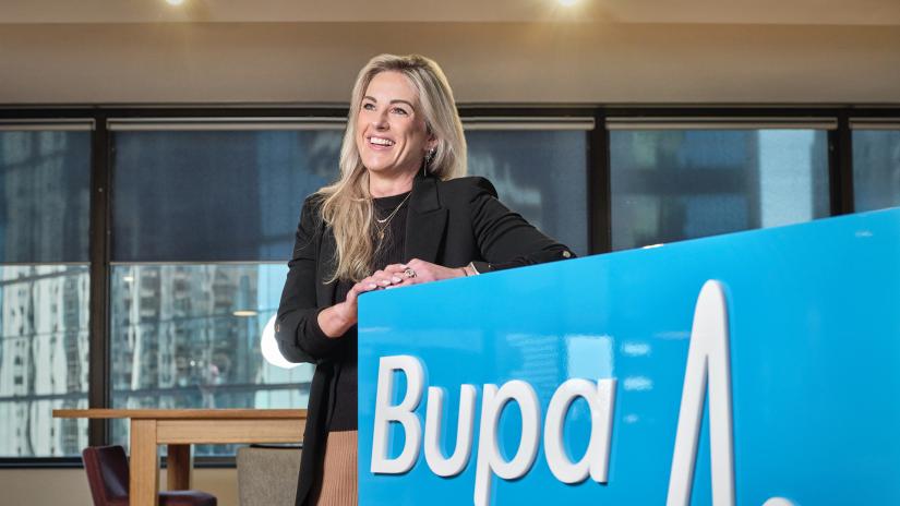 Danielle Handley in corporate wear stands behind BUPA signage