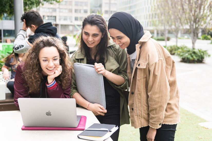 3 students smiling and looking at a laptop