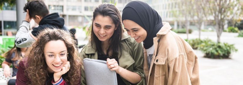 3 students smiling and looking at a laptop