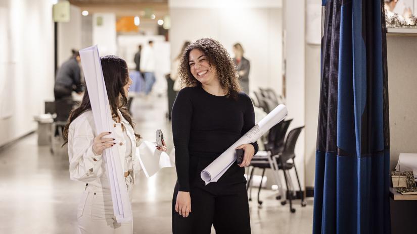 Two people chatting while holding large pieces of rolled up architectural drawings