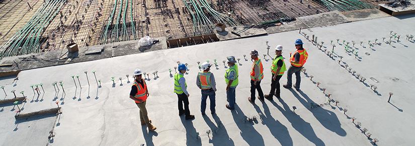 A group of construction workers in hard hats and safety vests standing together on a busy construction site.