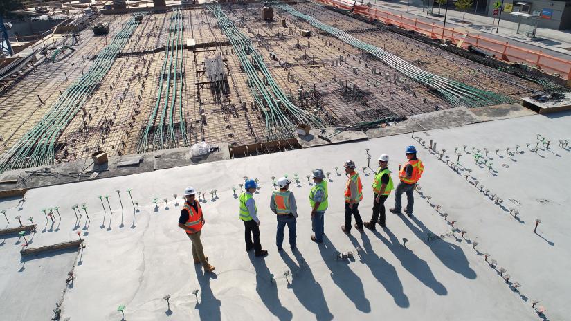 A group of construction workers in hard hats and safety vests standing together on a busy construction site.