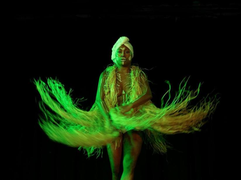 performance image of person in white dress and headress in green spotlight