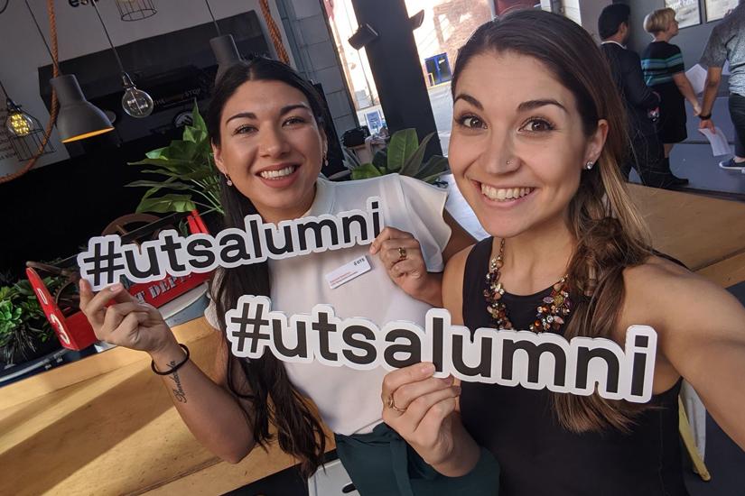 Two woman holding a #utsalumni sign and smiling